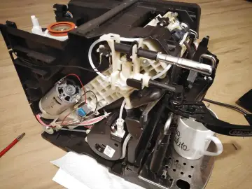 Rozłożony ekspres DeLonghi, który nie spienia mleka. Widoczne elementy mechanizmu, silnik i przewody.