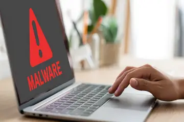 Czerwony wykrzyknik i napis "MALWARE" na ekranie laptopa, ostrzegający przed zagrożeniem, takim jak spyware.