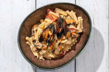 Piatto di pasta con fagioli e cozze, condita con pomodorini e una cremosa salsa.
