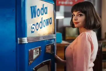 Kadr z filmu o Kalinie Jędrusik. Młoda kobieta w różowym swetrze przy sodostacji.