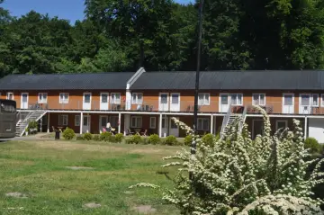 Hotel Stilo w otoczeniu zieleni. Dwa piętra drewnianych domków z balkonami i schodami.