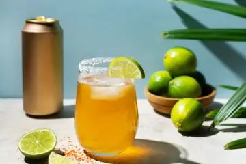 Orzeźwiający drink z Metaxą i colą, udekorowany limonką i solą, obok stoi złota puszka.