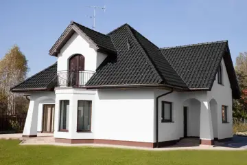 Biały dom z ciemnym dachem. Czy to kolor ral 7016? Elegancka biel ścian kontrastuje z grafitową dachówką.