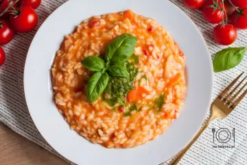 Pyszne risotto z pomidorami, udekorowane bazylią i pesto, czeka na talerzu. Obok świeże pomidorki i złoty widelec.