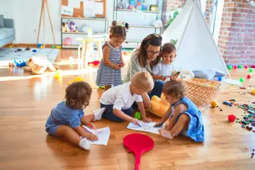Niania w Warszawie, opiekująca się grupą dzieci, które rysują na podłodze. Zastanawiasz się, ile zarabia niania w Warszawie?
