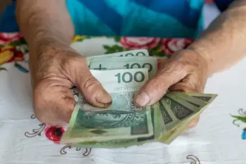 Dłonie starszej osoby liczą banknoty 100 zł. Może to być pomocne przy analizie 14 emerytura tabela.