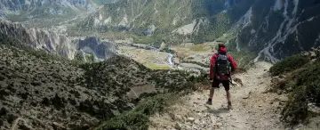 Widok na dolinę z góry. Turysta w czerwonej kurtce i plecaku zastanawia się, co zabrać w góry.