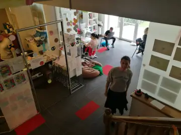 Wnętrze z elementami edukacji alternatywnej: dzieci i młodzież pracują, uczą się, bawią. Widać kolorowe dekoracje, tablice, wygodne siedziska.