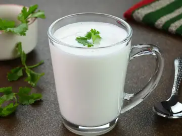 Szklanka pełna białego napoju, ozdobiona listkiem pietruszki. Zastanawiasz się, czym się różni kefir od maślanki?