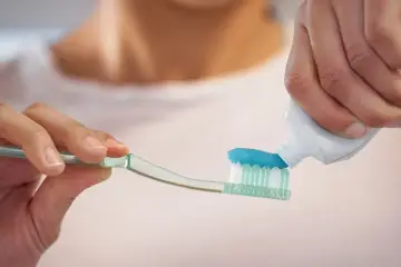 Nakładanie niebieskiej pasty do zębów z fluorkiem sodu na szczoteczkę.