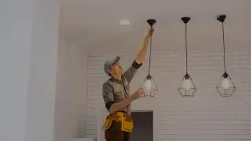 Elektryk montuje lampę wiszącą na suficie.