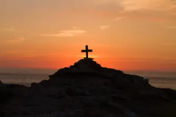 Kamienny krzyż na skalistym wzgórzu o zachodzie słońca, symbolizujący moment, kiedy umarł Jezus.