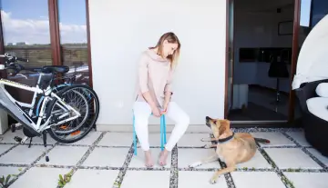 Katarzyna Kędzierska, w młodym wieku, siedzi na krześle, a jej pies leży obok. Obok stoi rower.