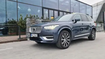 Elegancki, ciemnoszary Volvo XC90 T8 Recharge z polskimi tablicami rejestracyjnymi stoi przed nowoczesnym budynkiem z dużymi oknami.