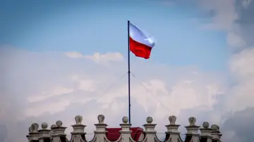 Biało-czerwona flaga powiewa na maszcie nad zabytkowym budynkiem. Wiatr rozwiewa ją, jakby niosła słowa o Polsce.
