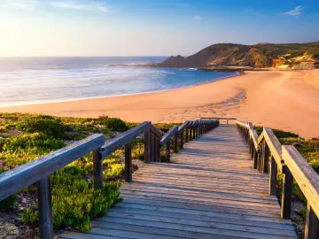 Drewniane schody prowadzą na piaszczystą plażę nad oceanem. To dowód, że Portugalia leży nad morzem, oferując piękne widoki.