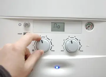 Dłoń reguluje pokrętłem pieca, przygotowując dom na nadchodzący sezon grzewczy. Na wyświetlaczu widnieje "110".