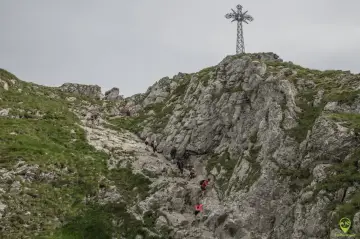 Grupa turystów wspina się po kamienistym zboczu w kierunku krzyża na szczycie. To idealny **Giewont dla początkujących**!