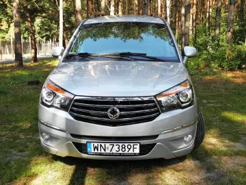 Srebrny SsangYong Rodius z przodu, zaparkowany na tle lasu.