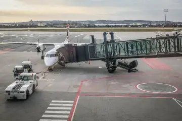 Samolot turbowentylatorowy podłączony do rękawa lotniskowego, gotowy do lotów krajowych. Na płycie lotniska widać pojazdy obsługi naziemnej.