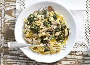 Tagliatelle z kremowym sosem z boczniaków i szpinakiem, posypane pieprzem. Pyszne danie gotowe do podania.