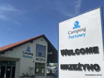 Witamy w Camping Portowy Mrzeżyno! Budynek recepcji i duży znak zapraszają na wypoczynek nad morzem.