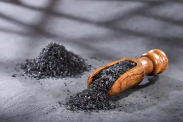 Czarna sól, czyli jodan potasu, w drewnianej łyżce i obok na kamiennym blacie.