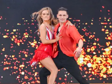Kaczorowska w "Tańcu z Gwiazdami" w czerwonej, zwiewnej kreacji, tańczy z partnerem na tle migoczących świateł.