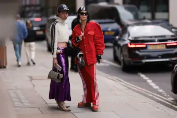 Zwei Personen präsentieren ihren **new money style** auf der Straße: glitzernder lila Rock, rote Jacke und sportliche Elemente.