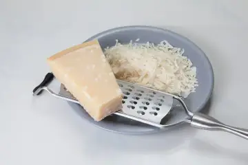 Kawałek parmezanu i starty ser na talerzu. Zastanawiasz się, czy parmezan można mrozić? Tak, można go mrozić, zachowuje wtedy smak.