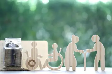 Skarbonka z monetami i drewniane figurki symbolizujące wsparcie dla osób starszych i niepełnosprawnych. Świadczenie wspierające punkty to szansa na lepsze jutro.