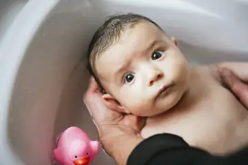 Niemowlę w wannie z różową kaczką. Czy można kąpać niemowlę z gorączką? Delikatna kąpiel w wannie.