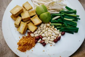 Składniki do sosu pad thai: smażone kostki tofu, orzeszki ziemne, szczypiorek, kiełki fasoli mung, limonki i płatki chili.