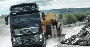 Ciężarówka Volvo FH16 750 z naczepą przewozi żółty wozidło przegubowe przez kamieniołom.