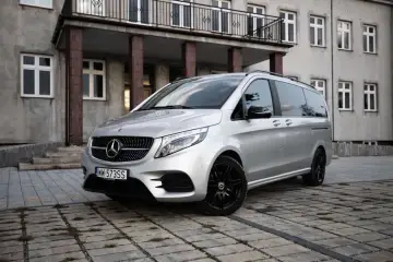 Srebrny Mercedes-Benz Klasy V z czarnymi felgami, zaparkowany przed budynkiem z balkonem.