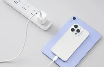 Biały telefon i tablet ładują się przez kabel. Wtyczka zasilająca jest podłączona do listwy zasilającej. ESD.