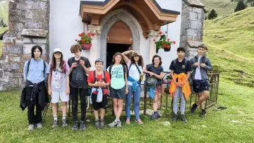 Groupe d'enfants en tenue de randonnée devant une petite église en montagne.