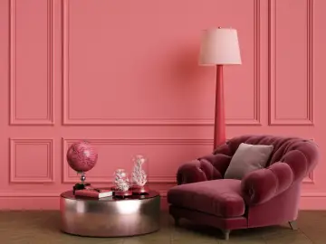Elegancki salon w odcieniach różu z tapicerowanym fotelem, stolikiem z globusem i lampą. Listwy przypodłogowe w kolorze ścian tworzą spójną całość.