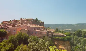 Village perché aux toits de tuiles roses, entouré de verdure. Au loin, des collines rappellent les vignes oubliées d'une Provence intemporelle.
