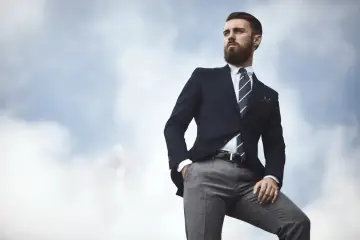 Elegancki mężczyzna w granatowej marynarce i szarych spodniach, z ręką w kieszeni, patrzy w dal. Stylowe granatowa marynarka stylizacje.