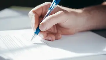 Dłoń pisze długopisem na dokumencie, być może podpisując pełnomocnictwo ogólne.
