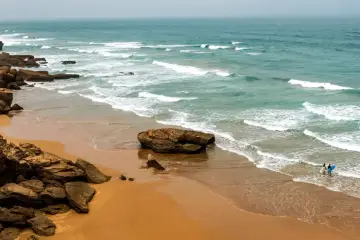 Maroko plaże: dwójka surferów wchodzi do wody z deskami, fale rozbijają się o skaliste wybrzeże.