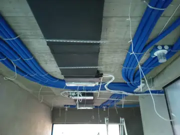 Instalacja rekuperacji w bloku: niebieskie rury wentylacyjne i czarny kanał wentylacyjny zamontowane na suficie.
