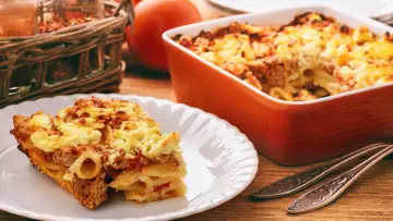 Zapiekanka makaronowa z mięsem mielonym w sosie śmietanowym, podana na talerzu i w naczyniu żaroodpornym.