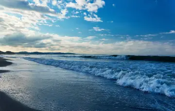Plaża nad Bałtykiem z falami i błękitnym niebem z chmurami.