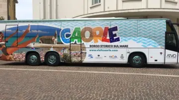 Bus turistico con grafica promozionale di Caorle, borgo storico sul mare. Immagini di spiaggia, mare e una donna in bikini.