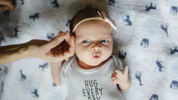 Uroczy 3 tygodniowy noworodek w body z napisem "HUG EVERY DAY", z delikatną opaską na głowie.