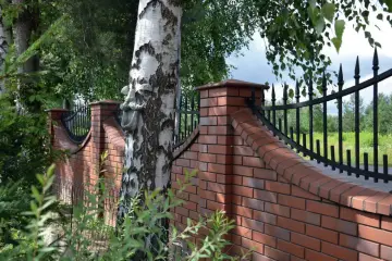Nowoczesne ogrodzenie z cegły z ozdobnym kutym elementem na pniu brzozy.