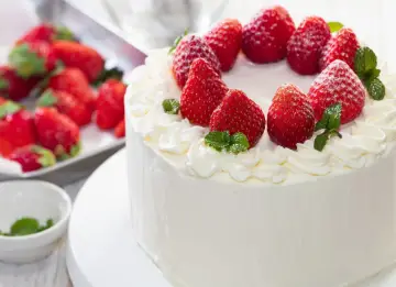 Puszysty tynk do tortu z mascarpone, ozdobiony świeżymi truskawkami i listkami mięty. Idealny na letnie przyjęcie.