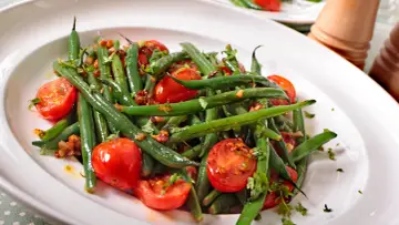 Insalata di fagiolini freschi con pomodorini ciliegino e erbe aromatiche, servita in un piatto bianco.
